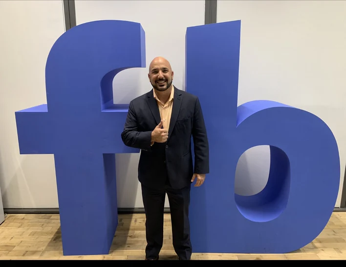 Ricardo Navalta standing in front of a large Facebook sign